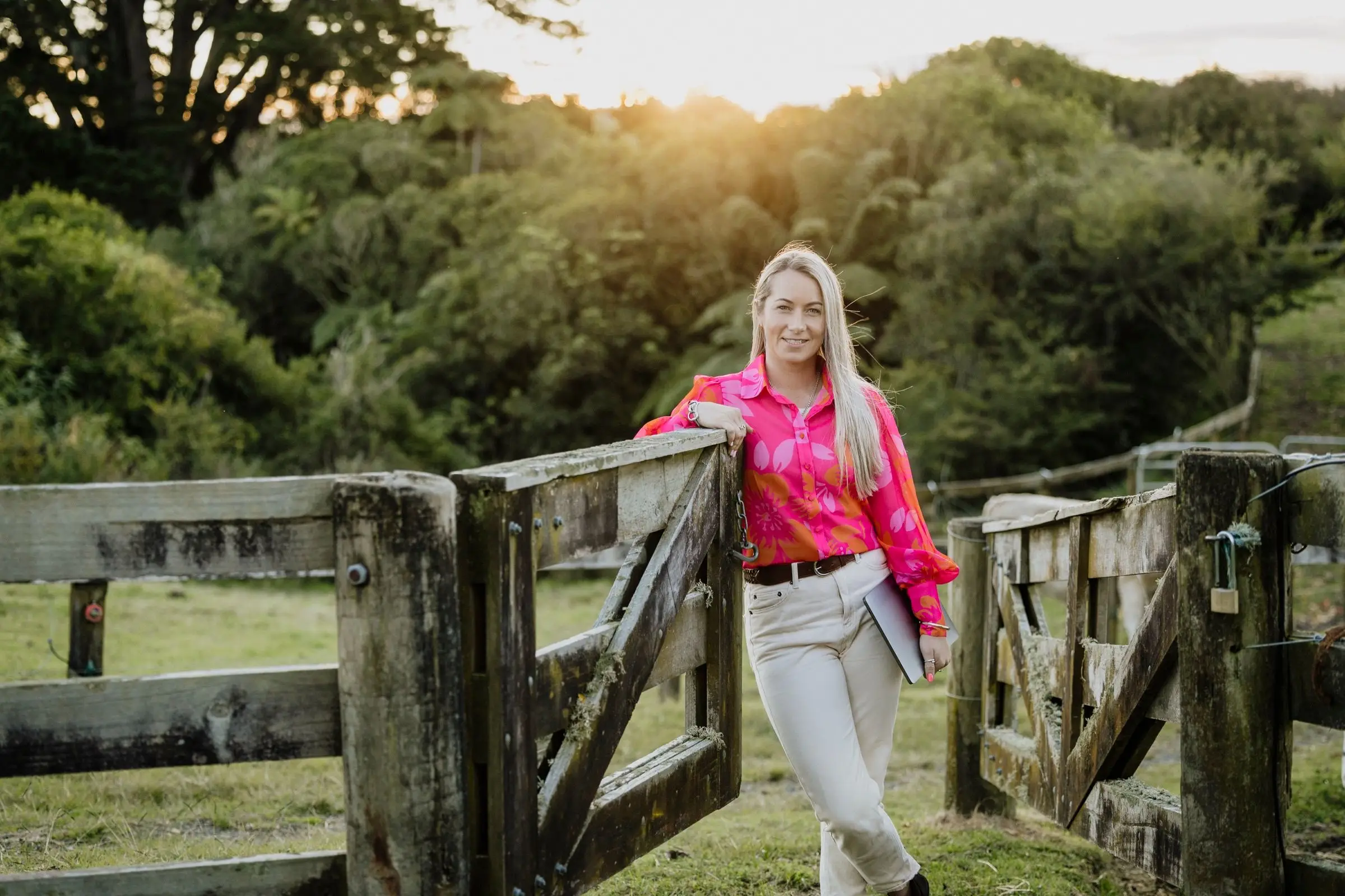 Paxton leaning on a weathered timber farm gate at sunset with native bush behind