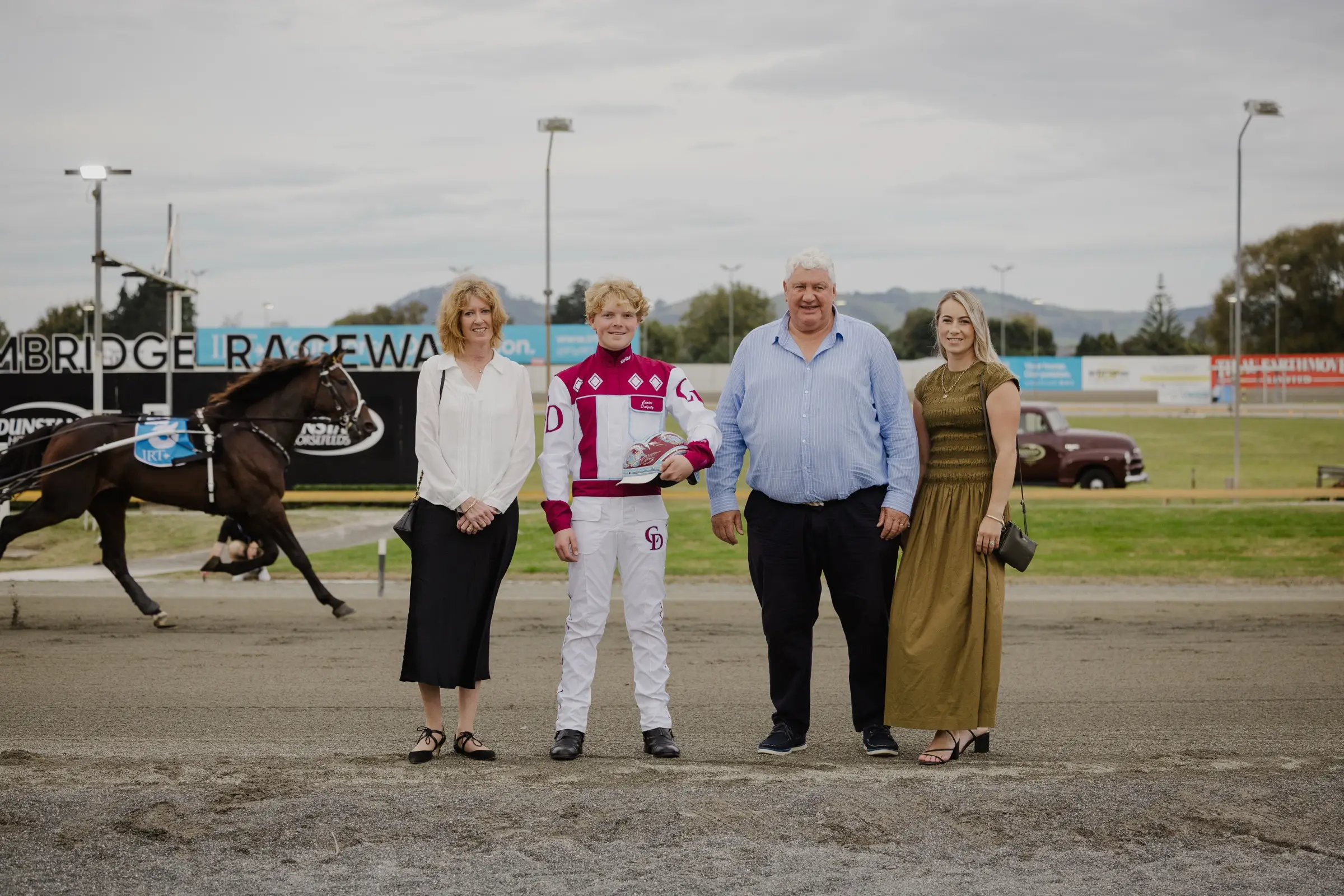 A presentation group at Cambridge Raceway with a junior driver in racing silks, a horse in motion behind them