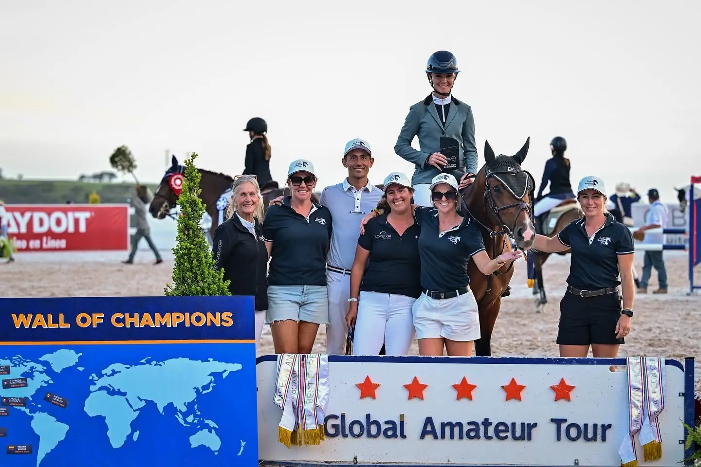 A Global Amateur Tour prizegiving with the tour team and a winning rider on horseback in front of the Wall of Champions