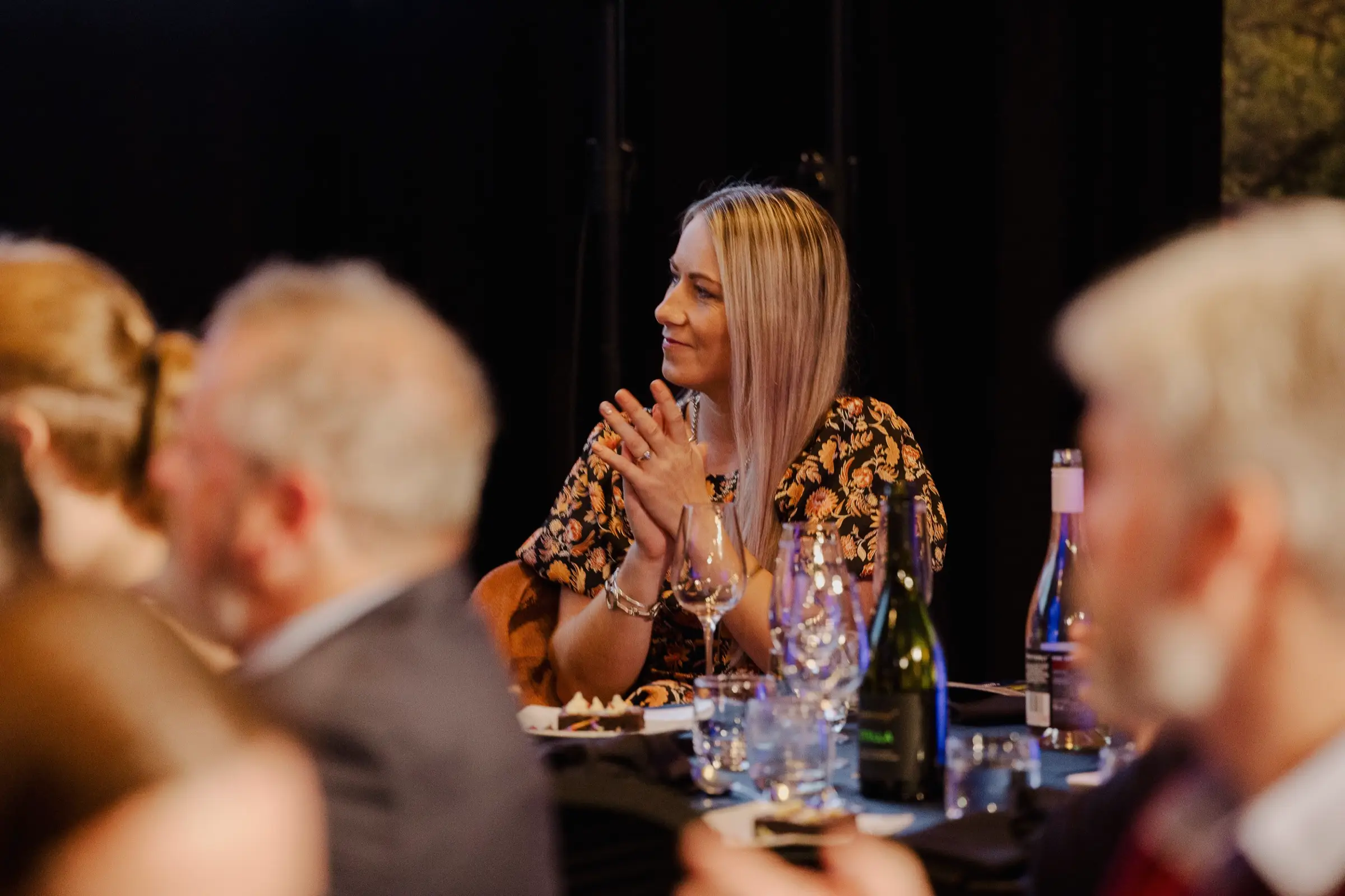 Paxton applauding at a table during an awards dinner, warm low light across the room