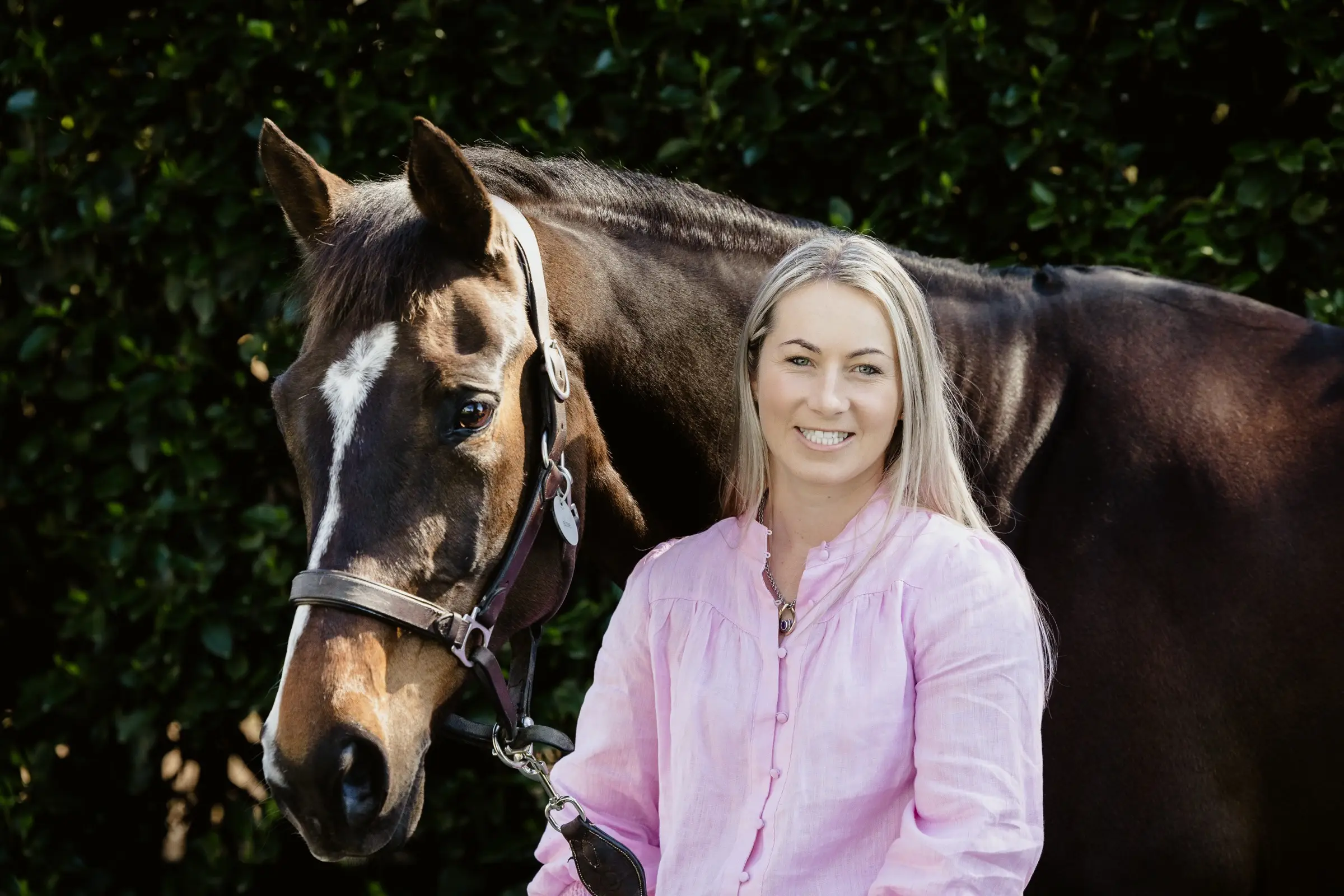 Paxton standing at the shoulder of a bay horse in front of a dark clipped hedge