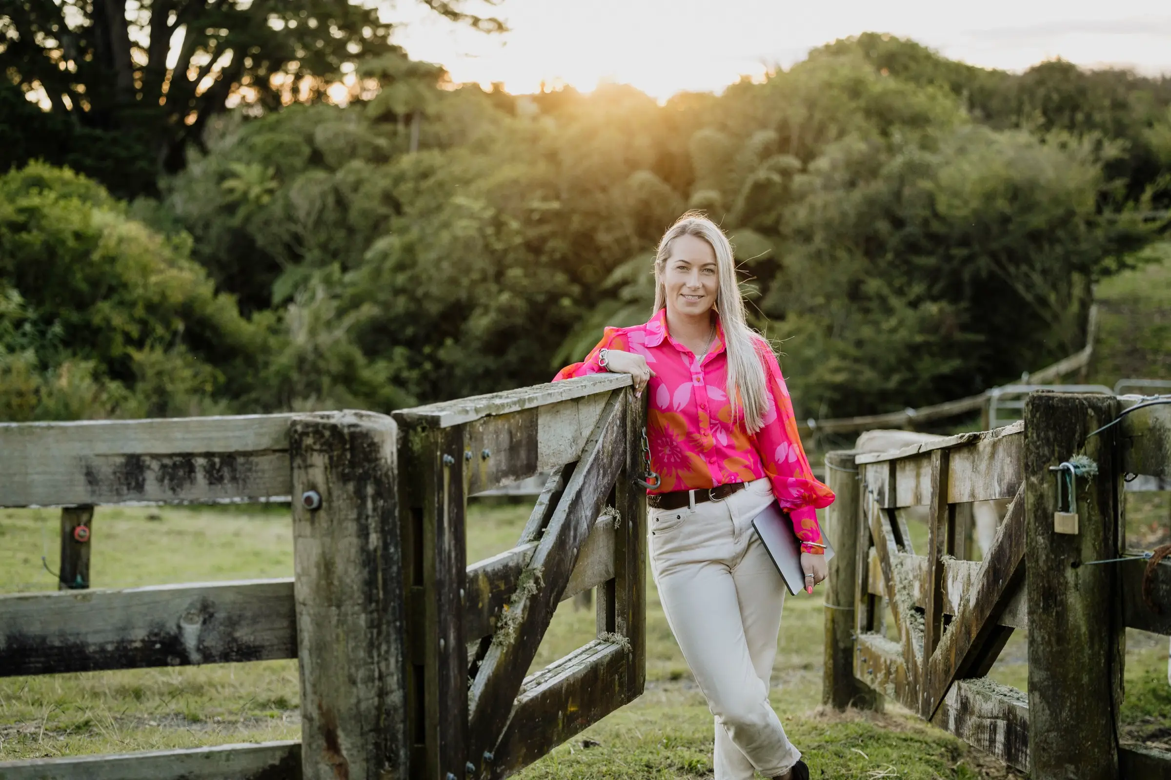 Paxton leaning on a weathered timber farm gate at sunset with native bush behind