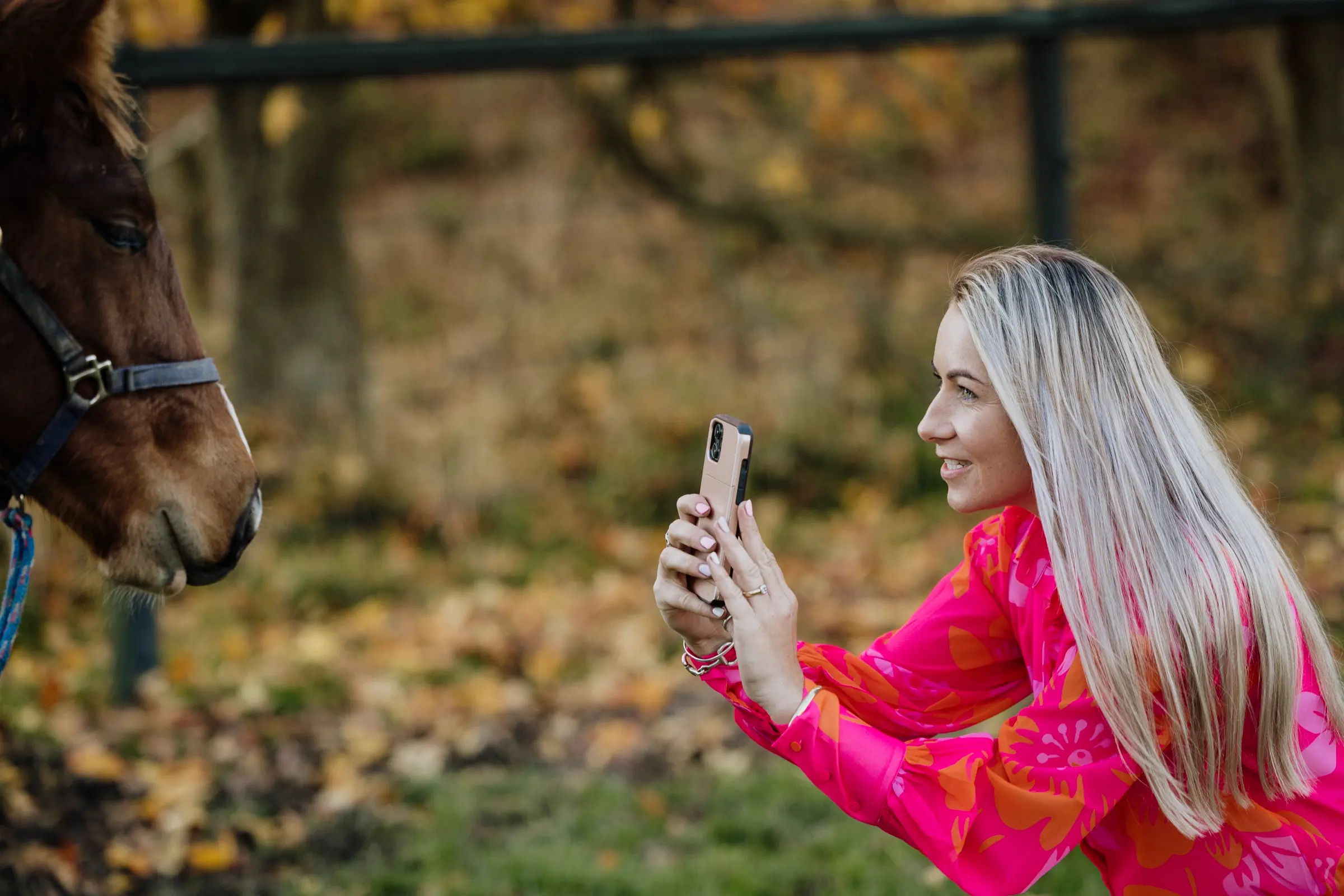 Paxton crouched at eye level with a horse, filming it on her phone