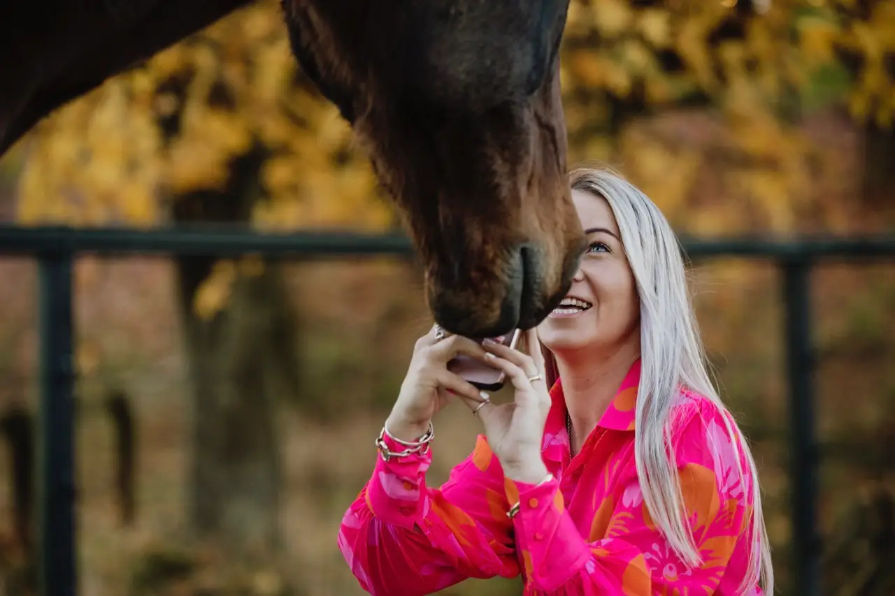 A horse reaching down to nuzzle Paxton's face while she laughs and looks up at it