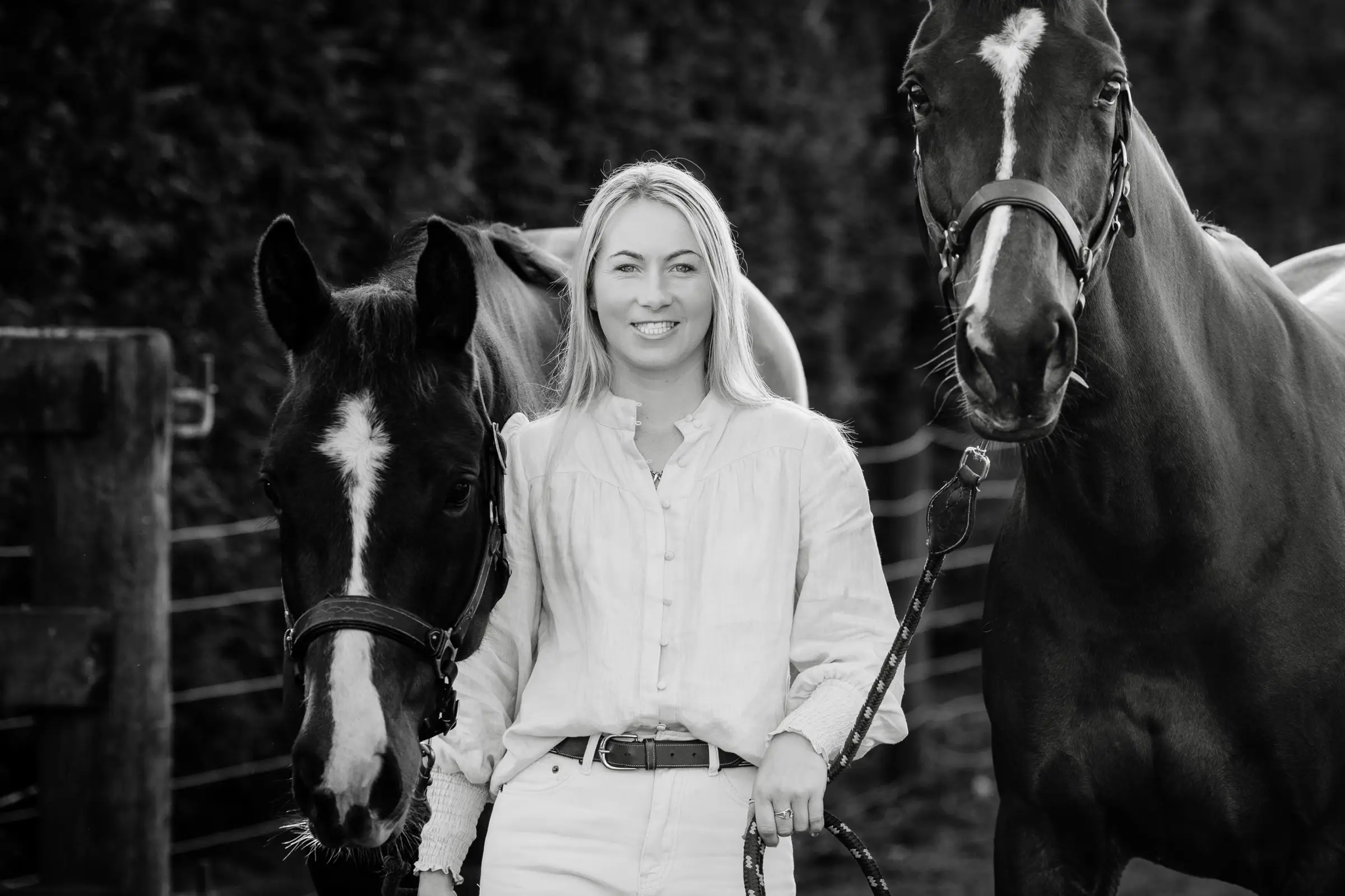 Black and white photograph of Paxton holding two horses on lead ropes in front of a farm gate