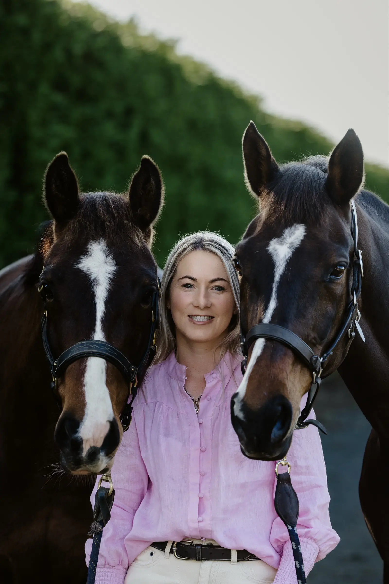 Paxton standing between two bay horses, one on each shoulder, both looking straight at the camera