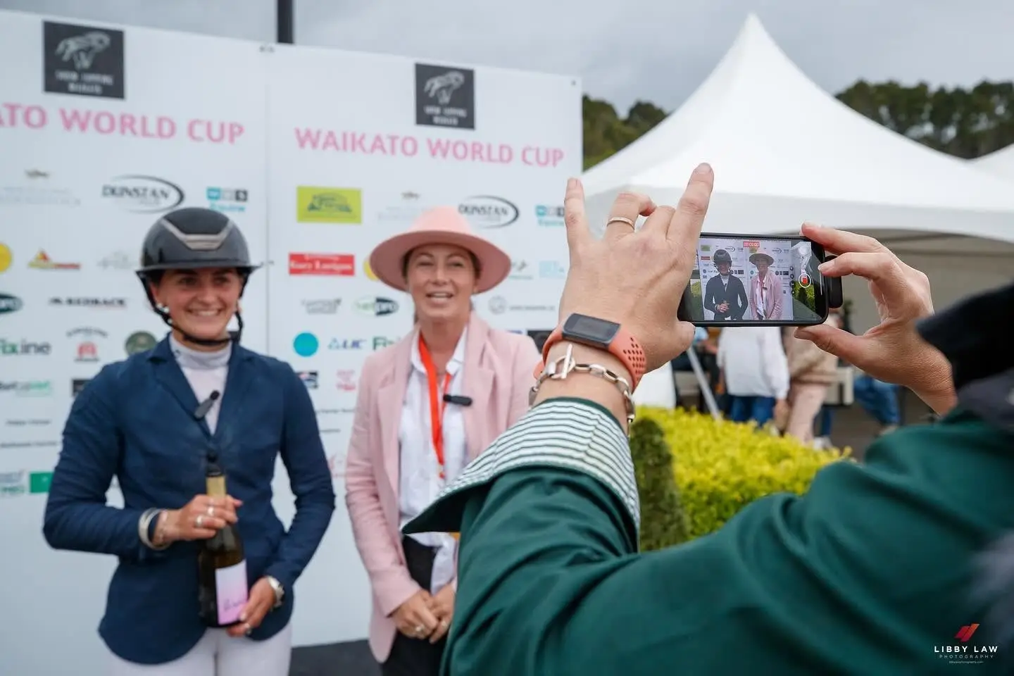 A phone held up filming a rider and an official at the Waikato World Cup prizegiving